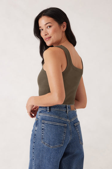 Woman wearing an olive green tank top and blue jeans against a white background